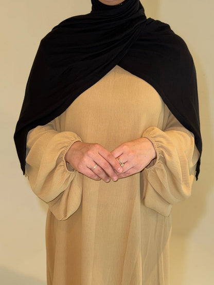 Nesthetics Abaya Malika aus Jazz Stoff mit Ballonärmeln in Beige, kombiniert mit schwarzem Hijab.