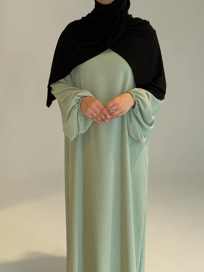Nesthetics Abaya Malika in Mintgrün aus Jazz Stoff mit Ballonärmeln und schwarzem Hijab.