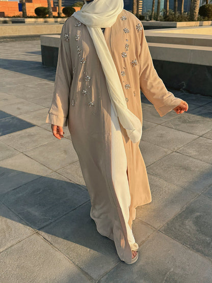 Nesthetics beige flowing abaya with intricate silver bead and sequin floral embellishments on the front and sleeves. Worn with a cream hijab.