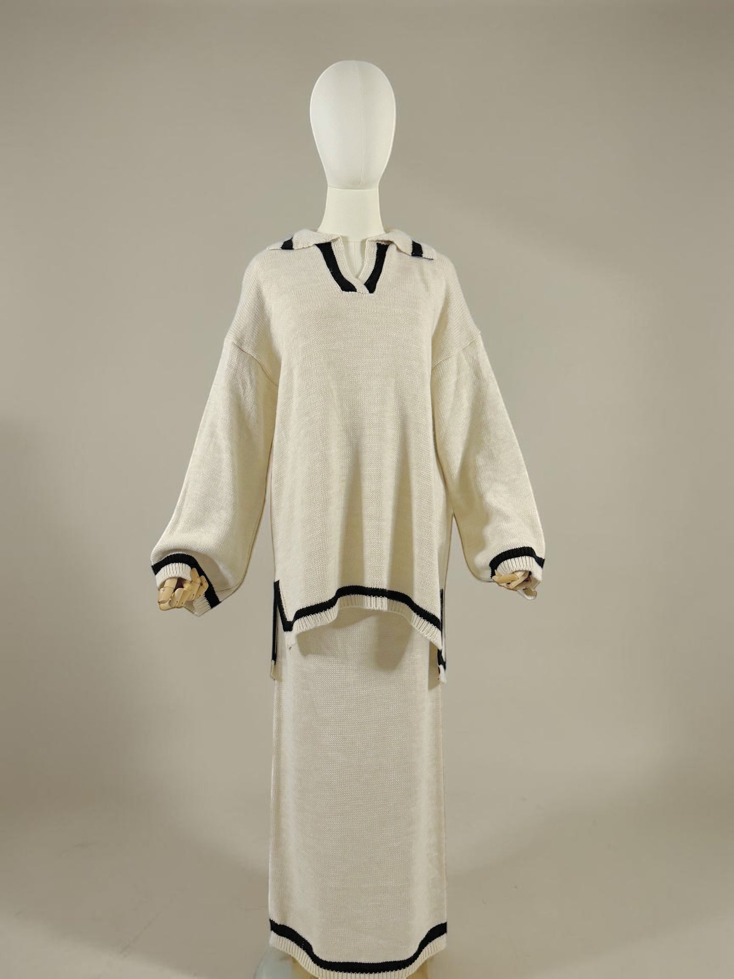 Nesthetics cream knit sweater with V-neck and black trim, paired with a matching midi skirt. Long sleeves with black cuffs.