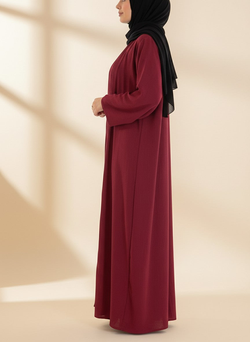Nesthetics dreiteilige Abaya Anisa in Burgundy aus Jazz-Stoff, getragen mit schwarzem Hijab in Seitenansicht