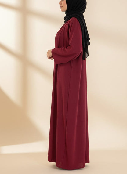 Nesthetics dreiteilige Abaya Anisa in Burgundy aus Jazz-Stoff, getragen mit schwarzem Hijab in Seitenansicht