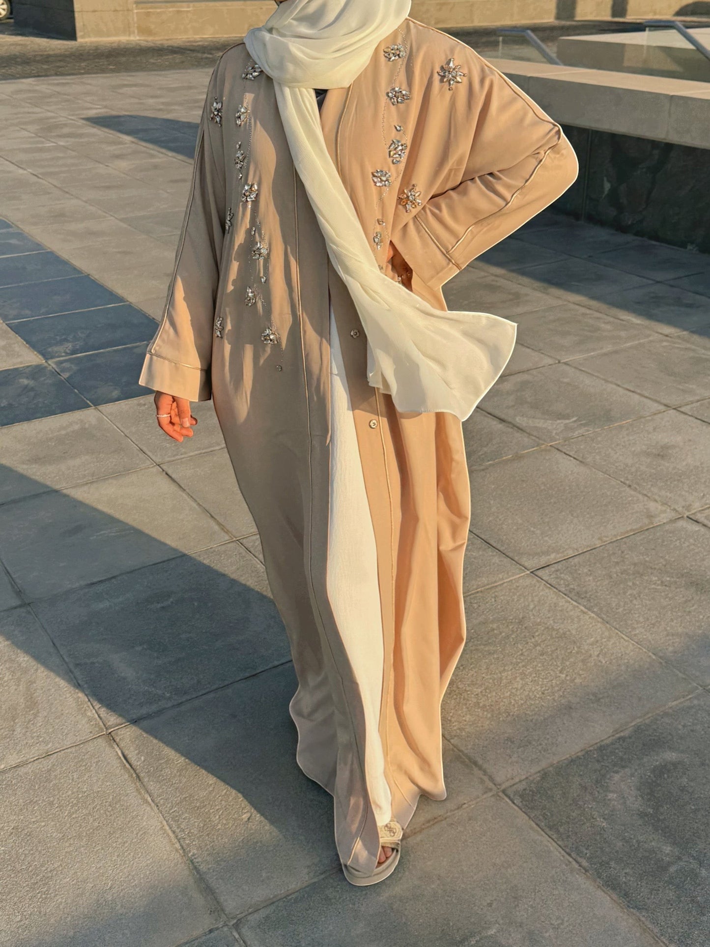 Nesthetics Prestige Abaya in beige with white contrasting panel and intricate crystal embellishments on the sleeves and chest. A flowing white hijab completes the elegant look.